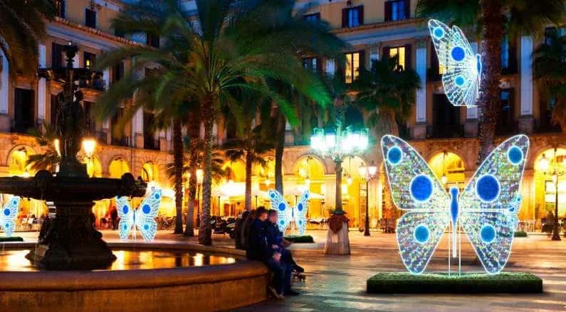 Palmiyeli meydanda büyük ve küçük mavi ışıklı kelebek figürleri, gece