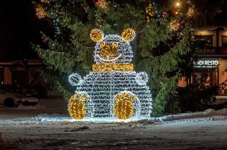Kardan adam figürünün yanında duran dev Noel Baba figürü, karlı çam ağaçları arasında