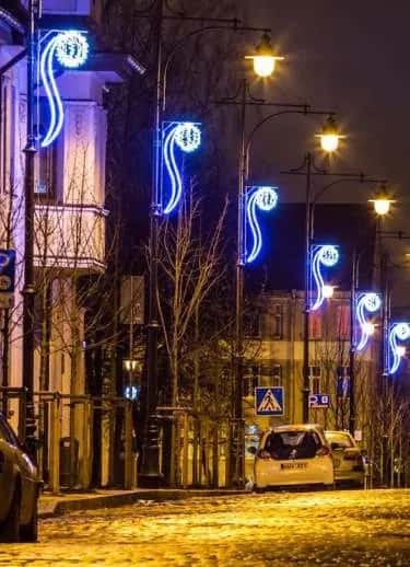 Mavi neon LED sarmal motifleriyle süslenmiş ağaçlı cadde direkleri, gece