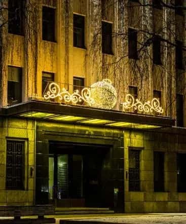 Otel girişi kanopisinde yatay altın LED yaprak sarmalı ve merkez küre süsü, gece