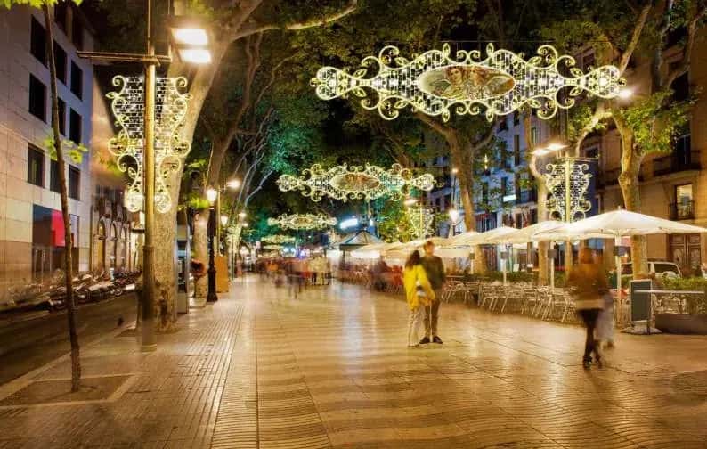 Ağaçlı yaya bulvarında ardışık asılı madalyonlu kristal sarkıtlar, gece kalabalığı altında