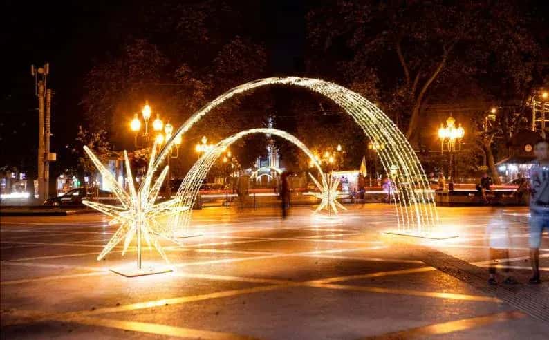 Gece meydanında art arda kurulmuş sıcak beyaz ışık yayları ve zemin yıldızları