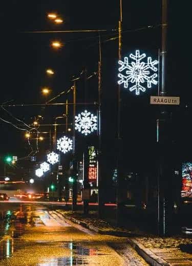 Islak asfaltlı cadde boyunca lamba direklerine monte edilmiş beyaz LED kar taneleri, gece