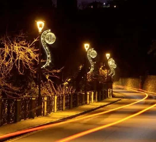 Kaldırım kenarı direklerine monte edilmiş altın LED sarmaşık ve küre motifleri, ağaçlı sokak