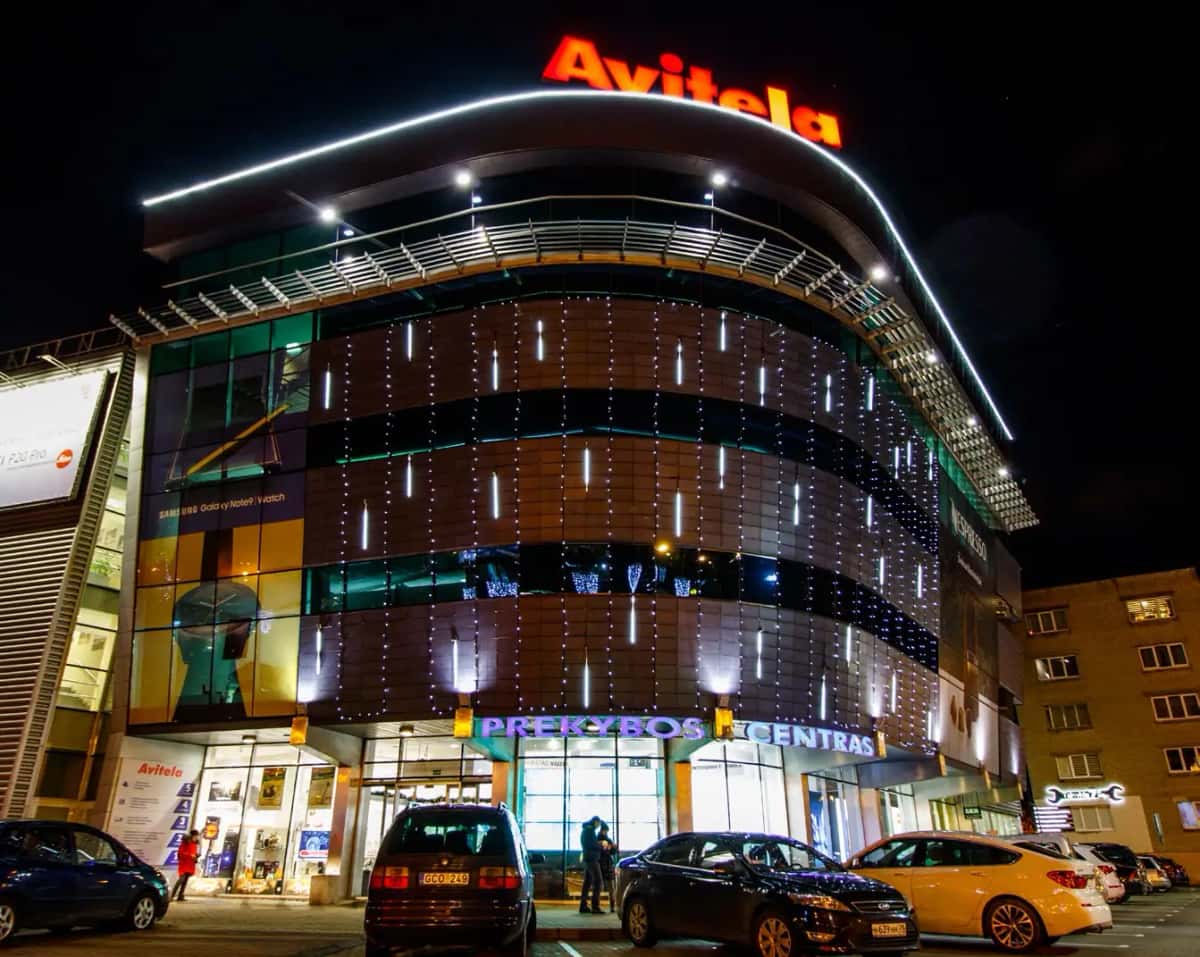 Gece alışveriş merkezi cephesinde dikey beyaz LED tüpler ve çatı hattı boyunca beyaz kontur