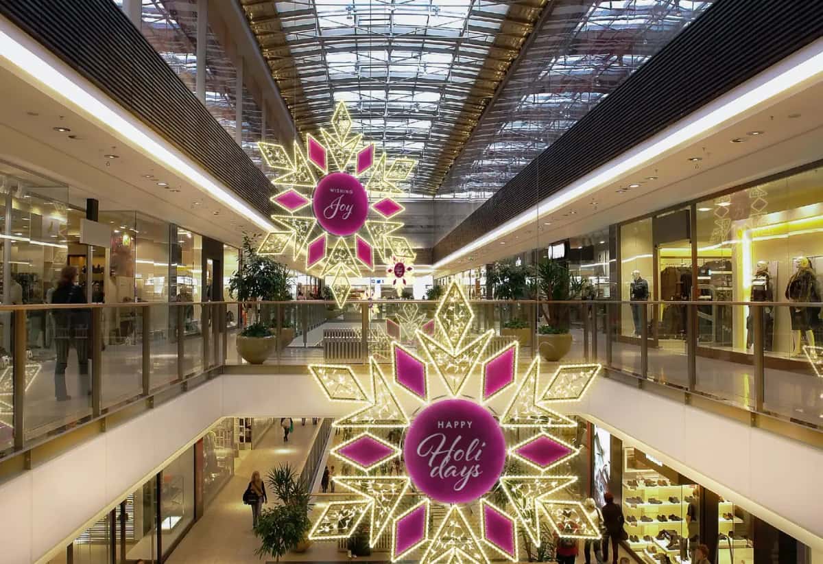 Alışveriş merkezi atriumunda asılı, ortası pembe yazılı altın LED kar taneleri