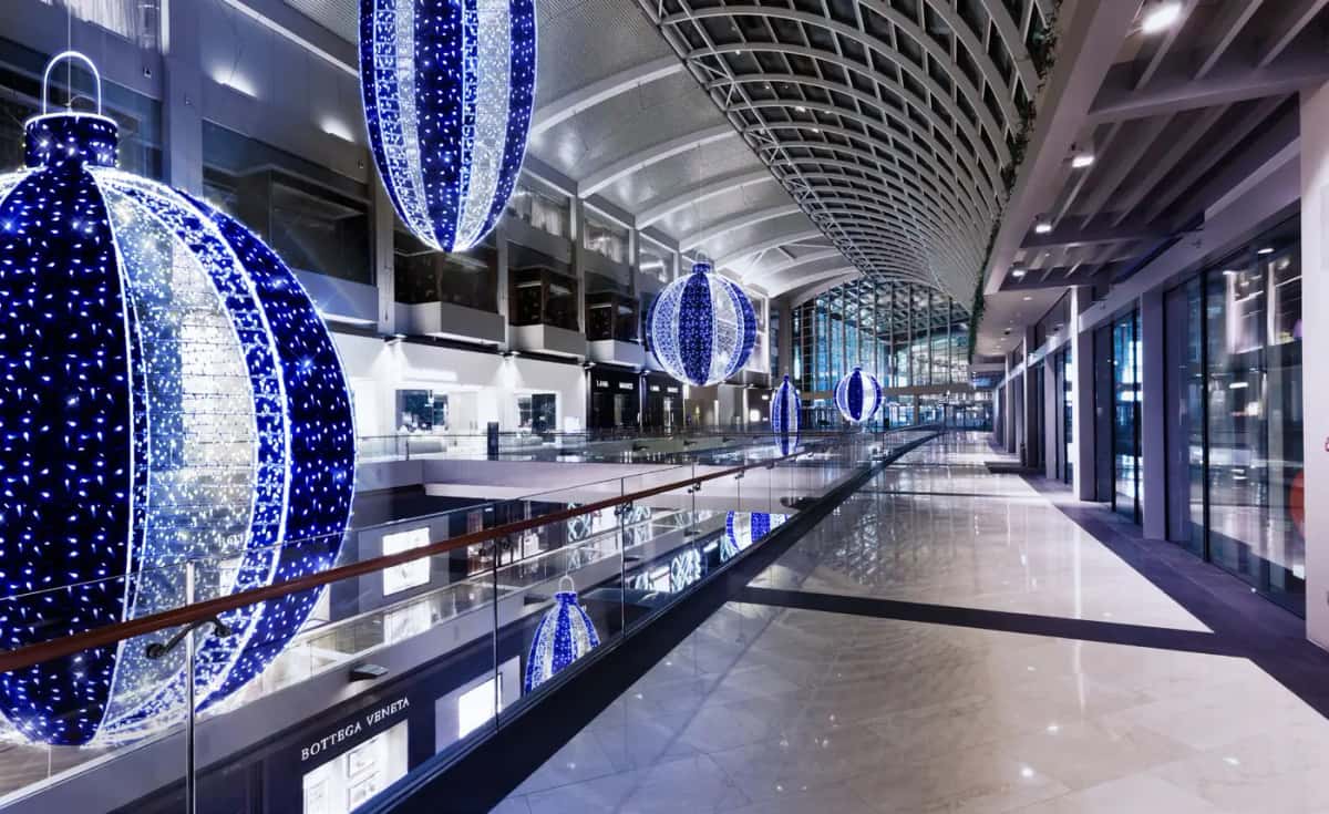 Alışveriş merkezi koridorunda tavandan sarkan mavi-beyaz dilimli büyük LED toplar