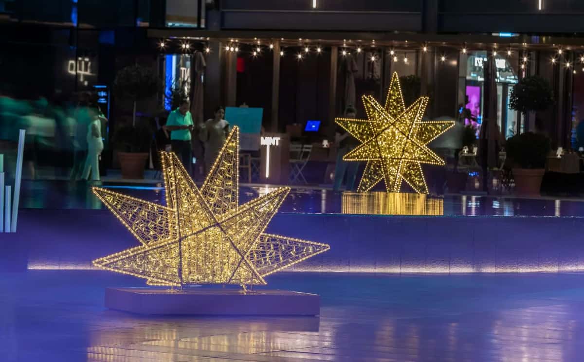 Alışveriş merkezi terasında buz pisti yanında iki altın sarısı 3 boyutlu LED yıldız, gece