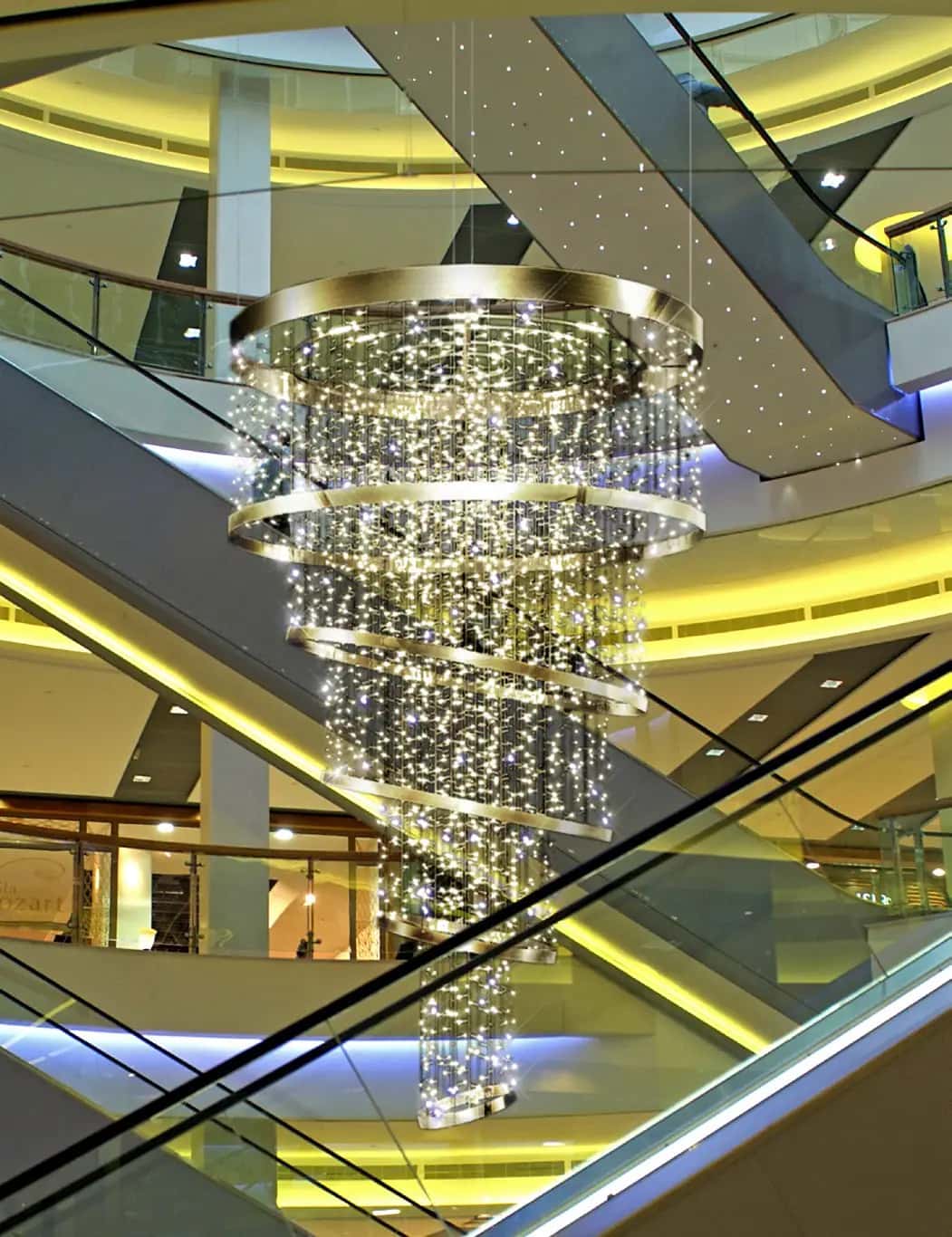 Yürüyen merdivenlerin üstünde spiral halkalı, sarkıtlı sıcak beyaz LED avize