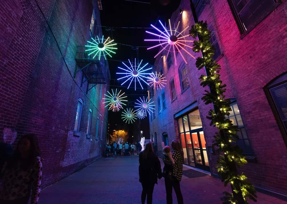 Tuğla duvarlı dar sokakta havada asılı çok renkli neon disk motifleri, gece