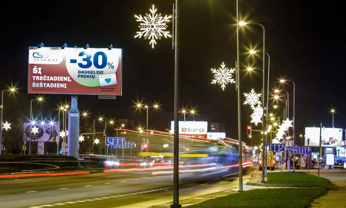 Bulvarda lamba direklerinde beyaz kar tanesi motifleri, reklam panosu görünüyor, gece