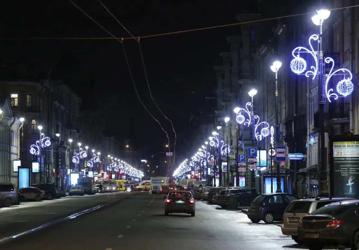 Geniş caddede sıralı lamba direklerinde mavi beyaz kıvrımlı motifler, gece