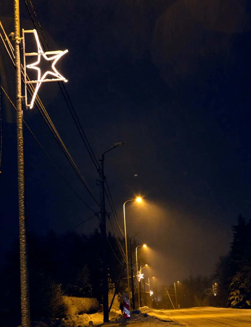 Karanlık yolda tel hatlı direğin üstünde beyaz yıldız çerçevesi, gece