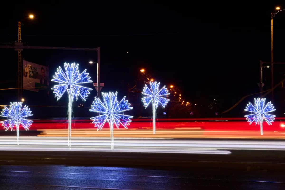 Işık izli geniş yol kenarında sıralanan mavi beyaz LED çiçek direkleri, gece