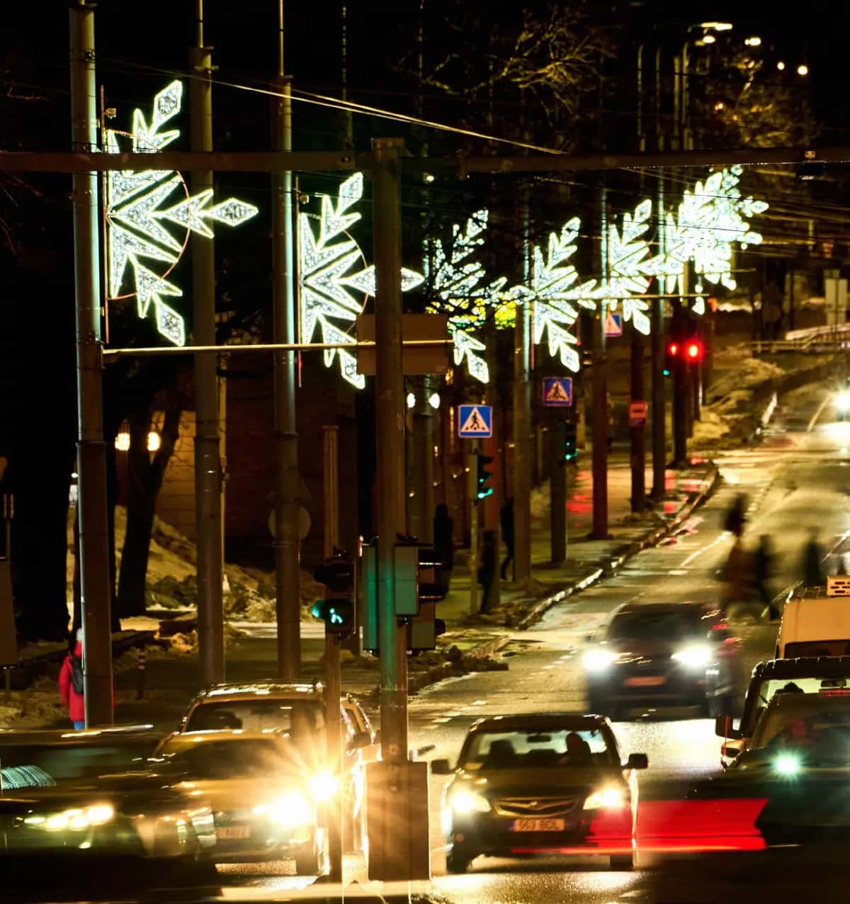 Trafikli caddede direklere dizili yeşilimsi beyaz kar tanesi motifleri, gece