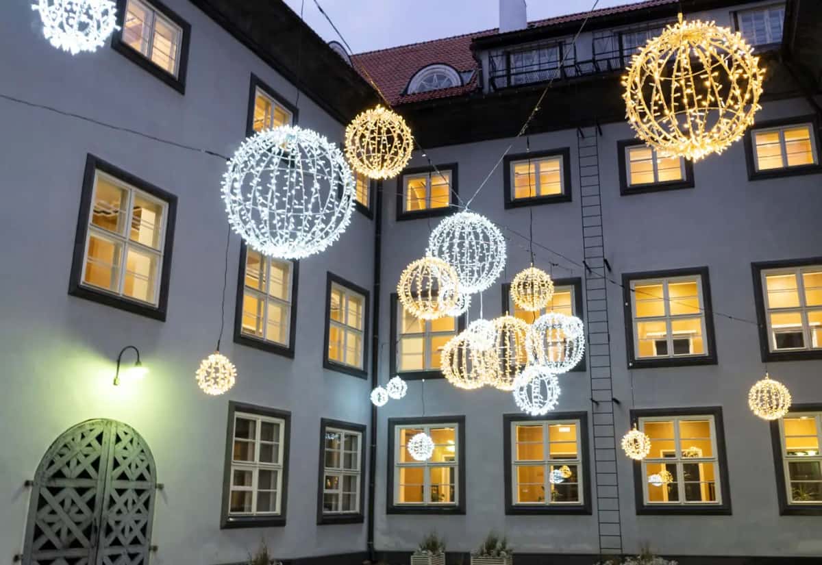 Pencereli binaların iç avlusunda havada asılı altın, beyaz ve mavi LED küreler, akşam