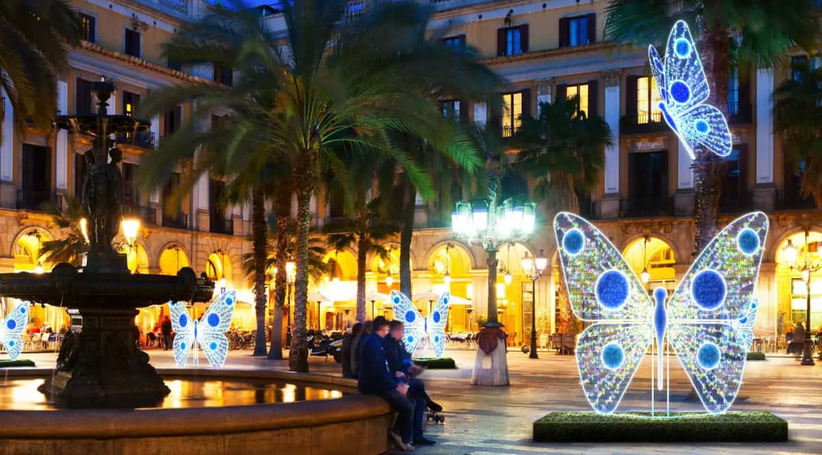 Çeşmeli ve palmiyeli meydanda mavi beyaz LED kelebek figürleri, tarihi binalar, gece