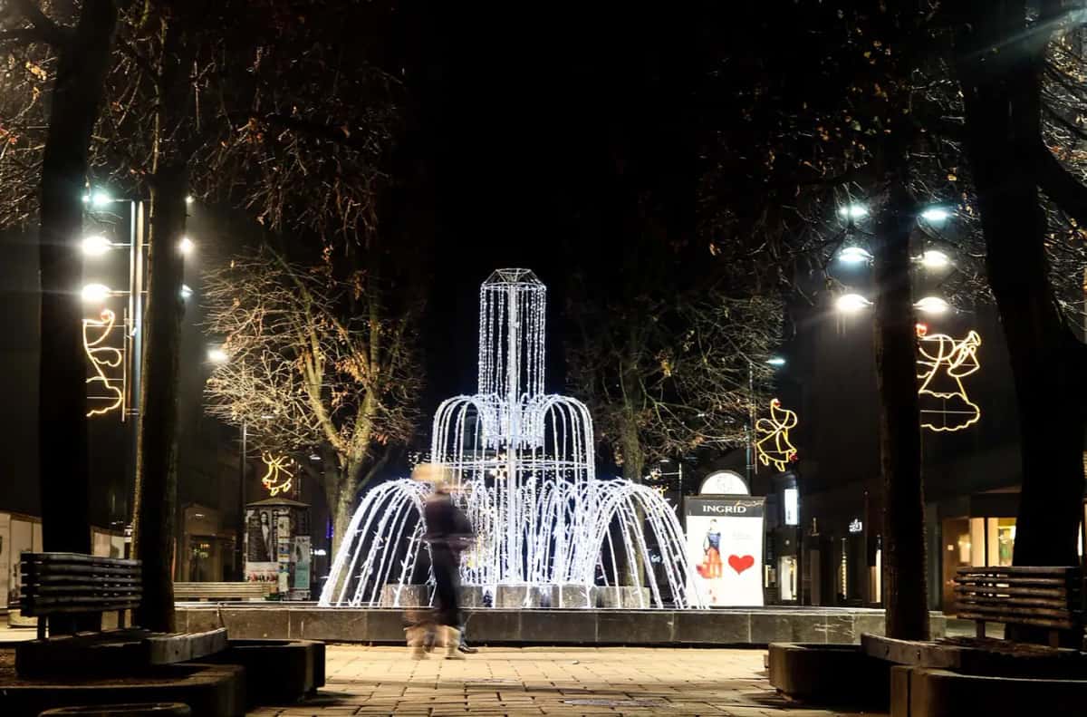 Ağaçların arasındaki meydanda soğuk beyaz LED ışık çeşmesi, banklar, gece