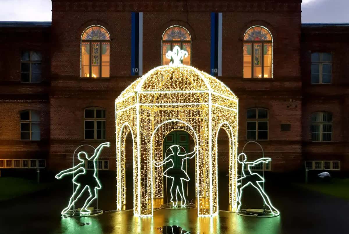 Tuğla bina önünde sıcak beyaz LED köşk ve çevresinde yeşil dans eden figürler, gece