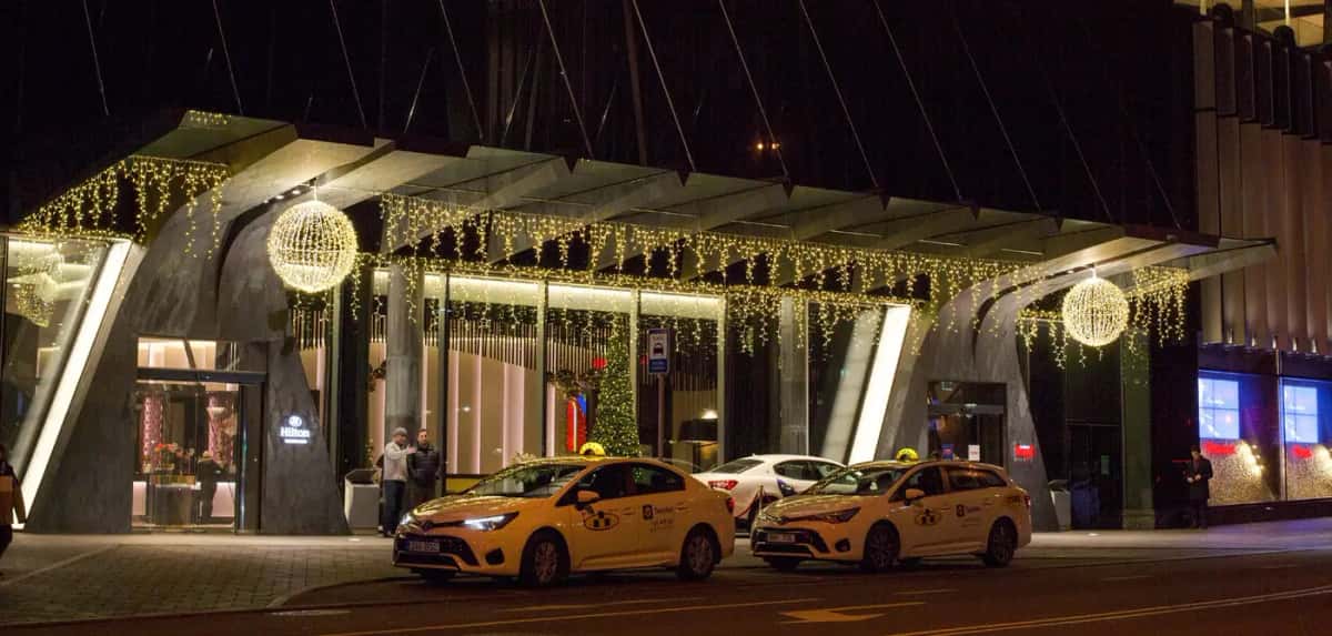 Gece otel girişi saçaklarında sıcak beyaz saçak LED ve asılı ışıklı toplar, önde taksiler