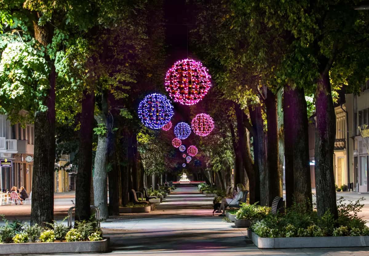 Ağaçlı yürüyüş yolunun üstünde asılı pembe ve mavi LED toplar, gece