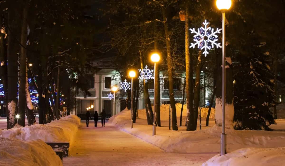 Karlı park yolunda lamba direğinde beyaz kar tanesi motifi, gece