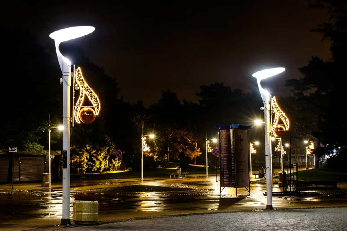 Parkta modern lamba direklerinde altın nota biçimli motifler, ıslak zemin, gece