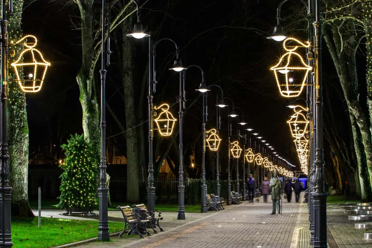 Parkta yürüyüş yolu boyunca lamba direklerine takılı altın renkli LED fener motifleri, gece