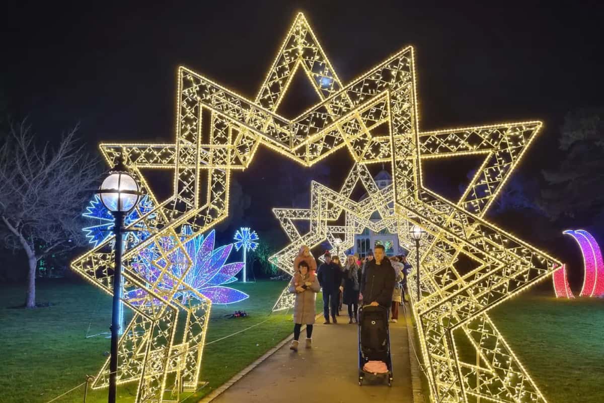 Park yolunda sıcak beyaz ışıklı yıldız biçimli kemer, altından geçen ziyaretçiler, gece