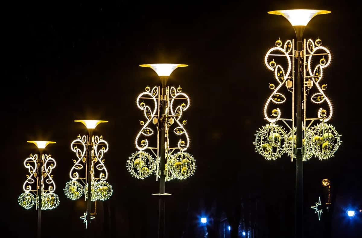 Dört lamba direğinde altın kıvrımlı motifler ve ışıklı küreler, gece