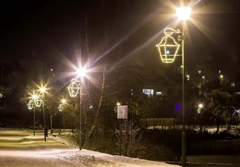 Karlı bir yol boyunca direklere monte edilmiş altın LED fener figürleri, gece
